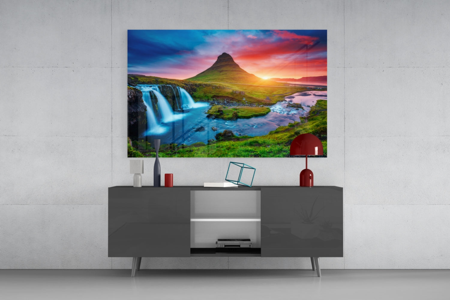 Glass wall art displaying Icelandic waterfall and mountain at sunset, mounted above gray media console in modern living room setting.