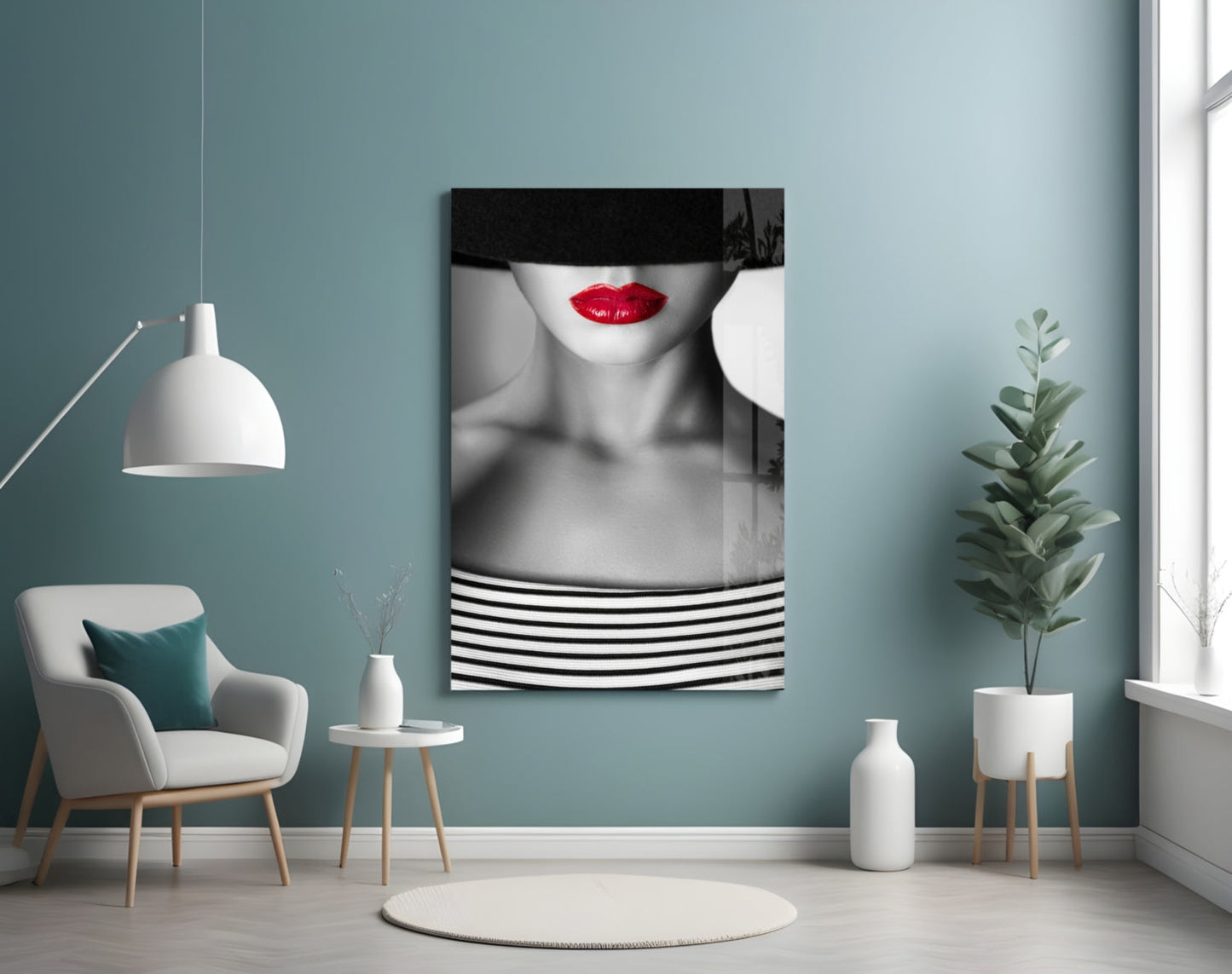 Black and white portrait with red lips and striped clothing displayed on turquoise wall above cream armchair with plant.