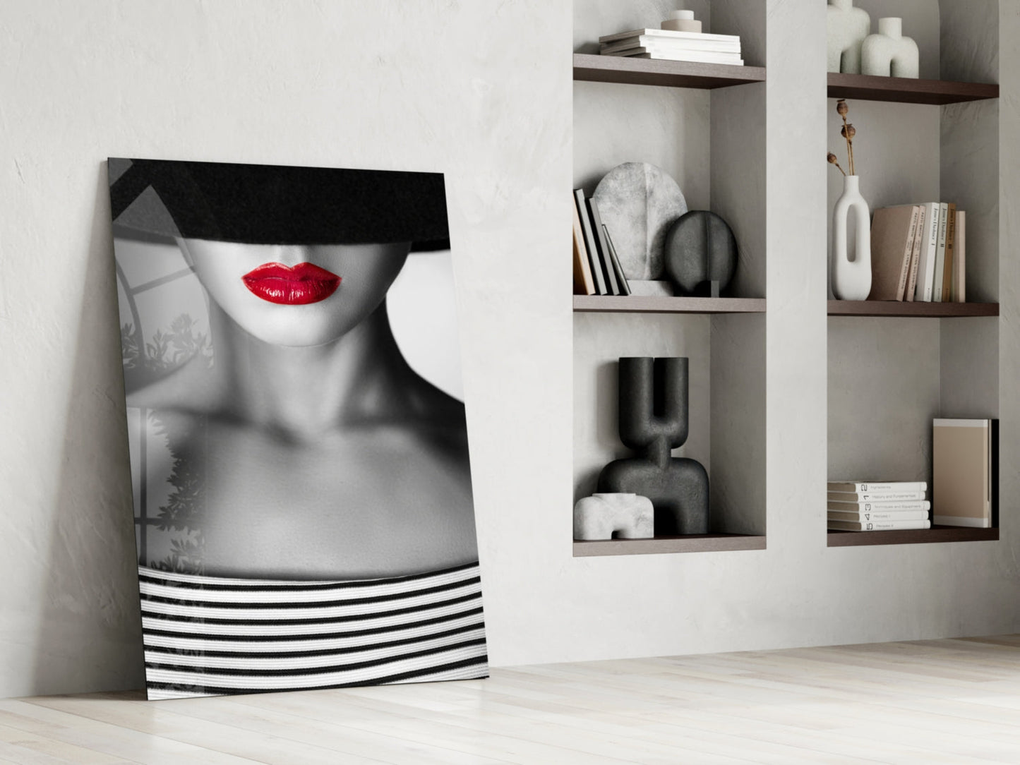 Modern interior display showing black and white portrait glass art with red lips leaning against white wall beside wooden shelving with decorative objects.