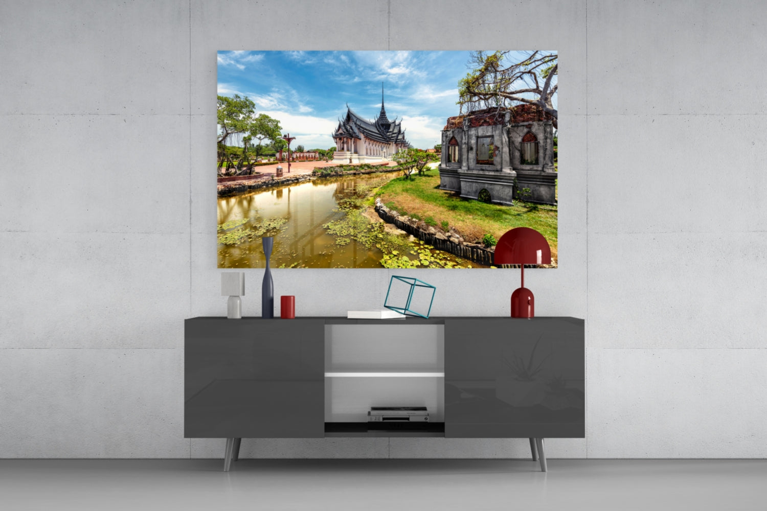Glass wall art depicting a Thai temple complex with pond and ruins displayed above a dark gray media console in a modern interior setting.