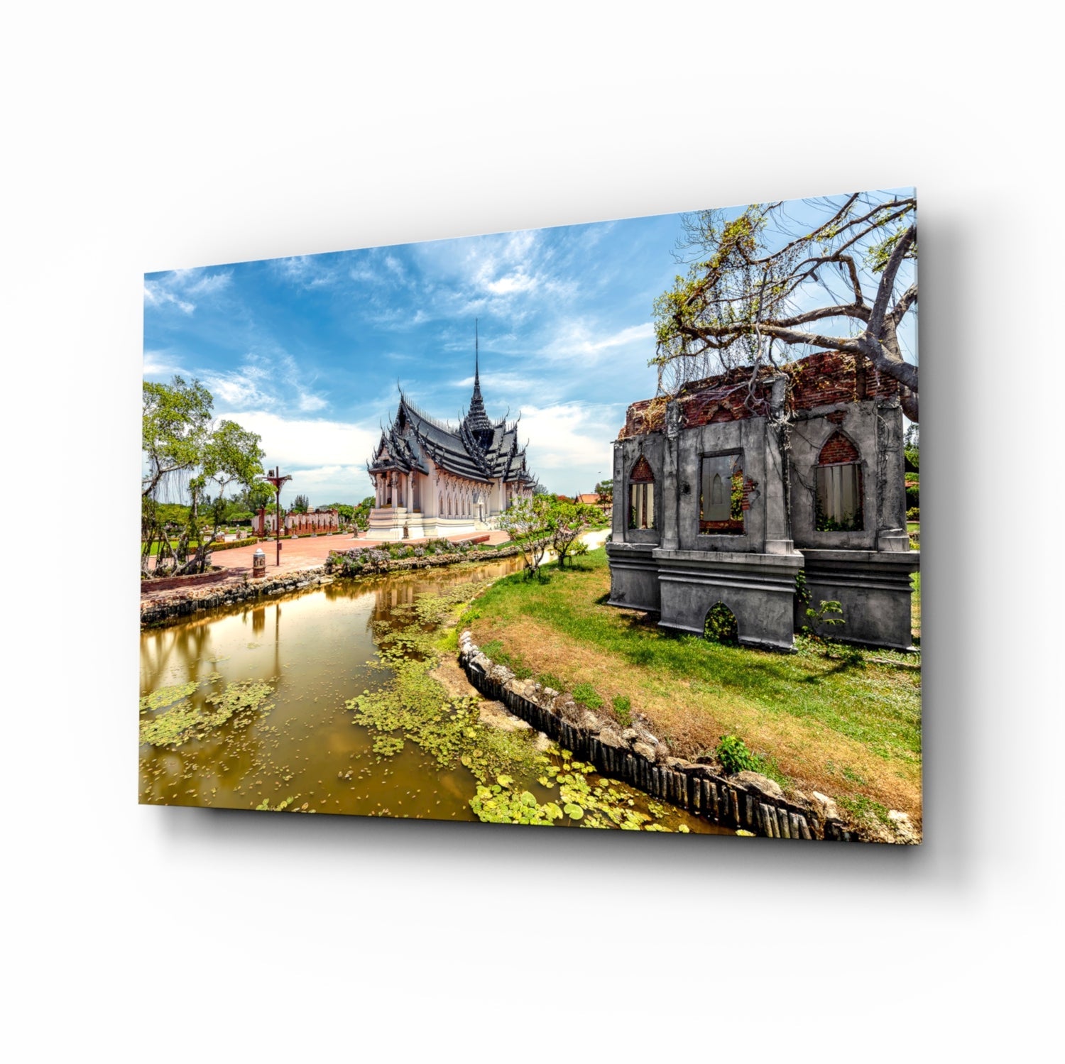 Glass wall art displaying a Thai temple with ornate roofs beside a reflective pond and weathered stone structure under blue sky.