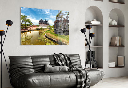 Glass wall art depicting a Thai temple beside a water canal with blue sky, displayed above a black leather sofa in a modern living room.