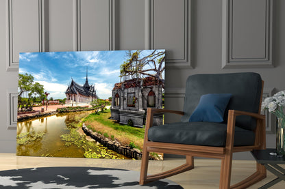 Small Village Glass Wall Art displaying Thai temple architecture with water canal and historic building, displayed in modern living room beside wooden chair.