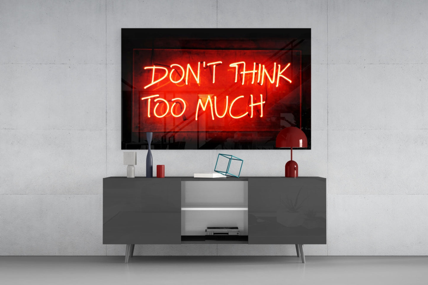 Red neon "Don't Think Too Much" sign displayed on wall above gray media console with decorative items.