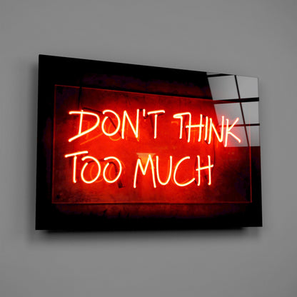 Red neon sign reading "DON'T THINK TOO MUCH" mounted on black framed glass panel against gray wall.