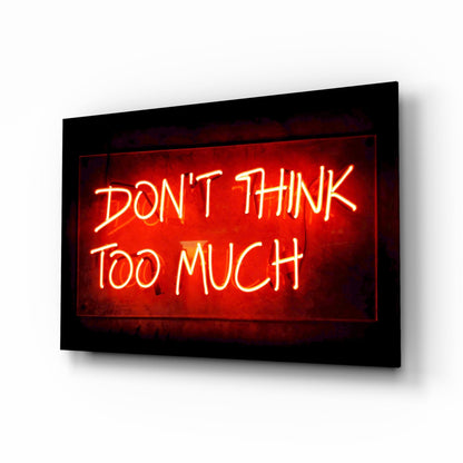 Red neon sign reading "DON'T THINK TOO MUCH" mounted on black framed glass wall art, angled perspective view.
