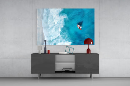 Aerial view glass art displaying turquoise ocean waves and red fishing boat mounted above dark media console with red decor accents.