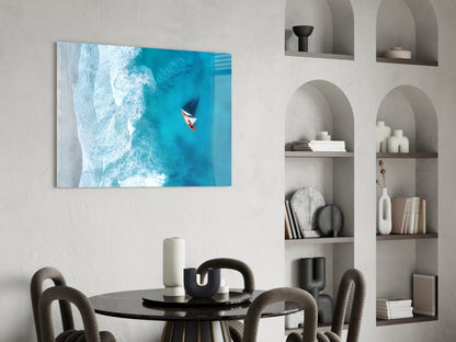 Aerial view glass art displaying turquoise ocean waves and small sailboat mounted above dining table in modern interior.