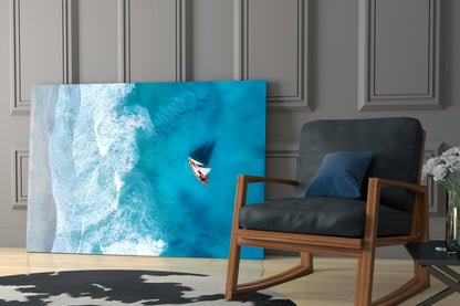 Aerial view glass art depicting turquoise ocean waves and red boat displayed in modern living room next to wooden chair.