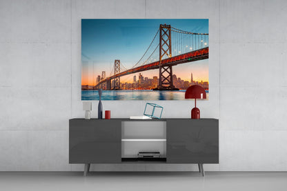 San Francisco Bay Bridge glass wall art mounted above gray media console displaying sunset cityscape with red accents.