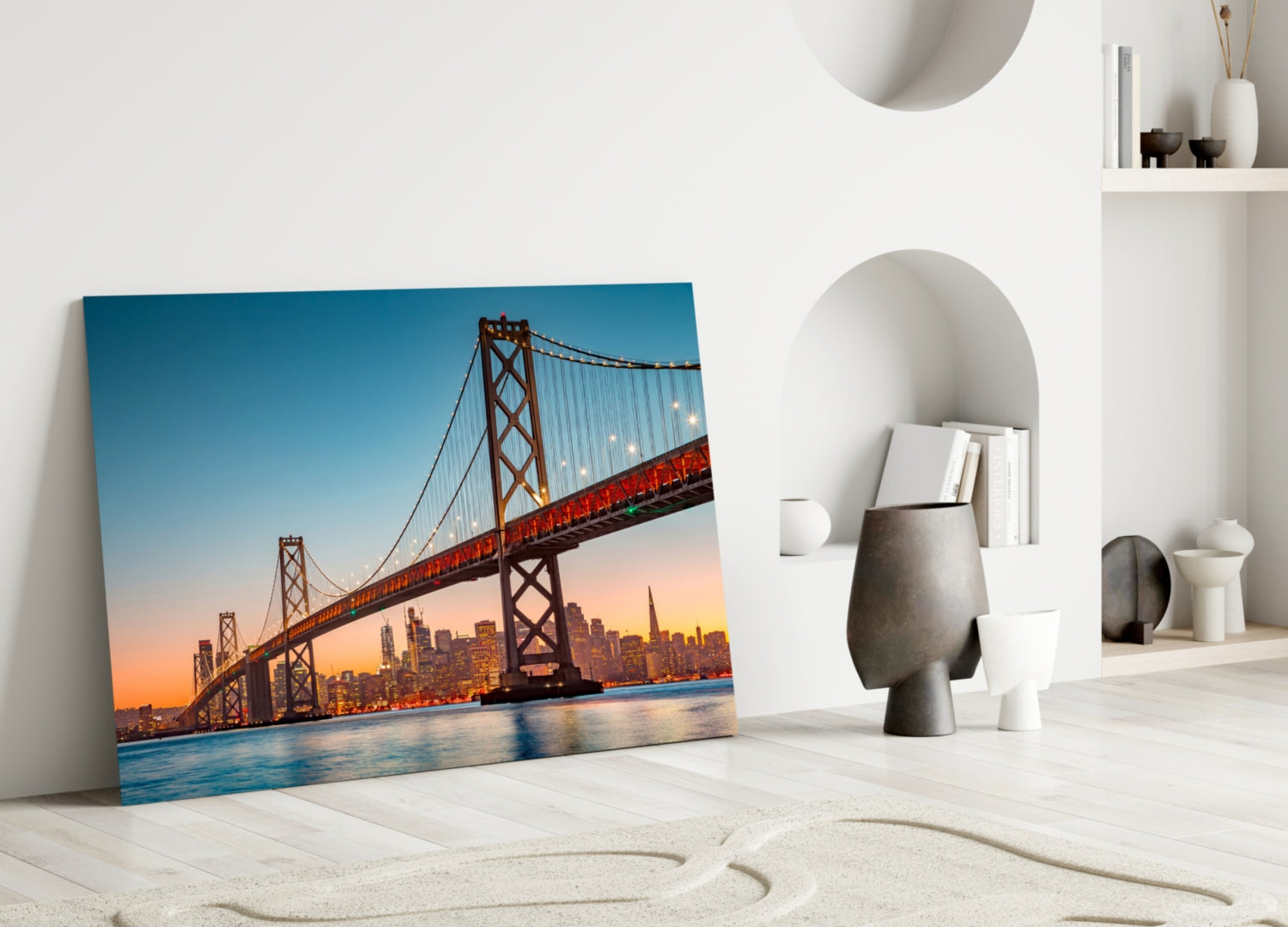 Glass wall art of the Bay Bridge at sunset leaning against white wall beside decorative objects.