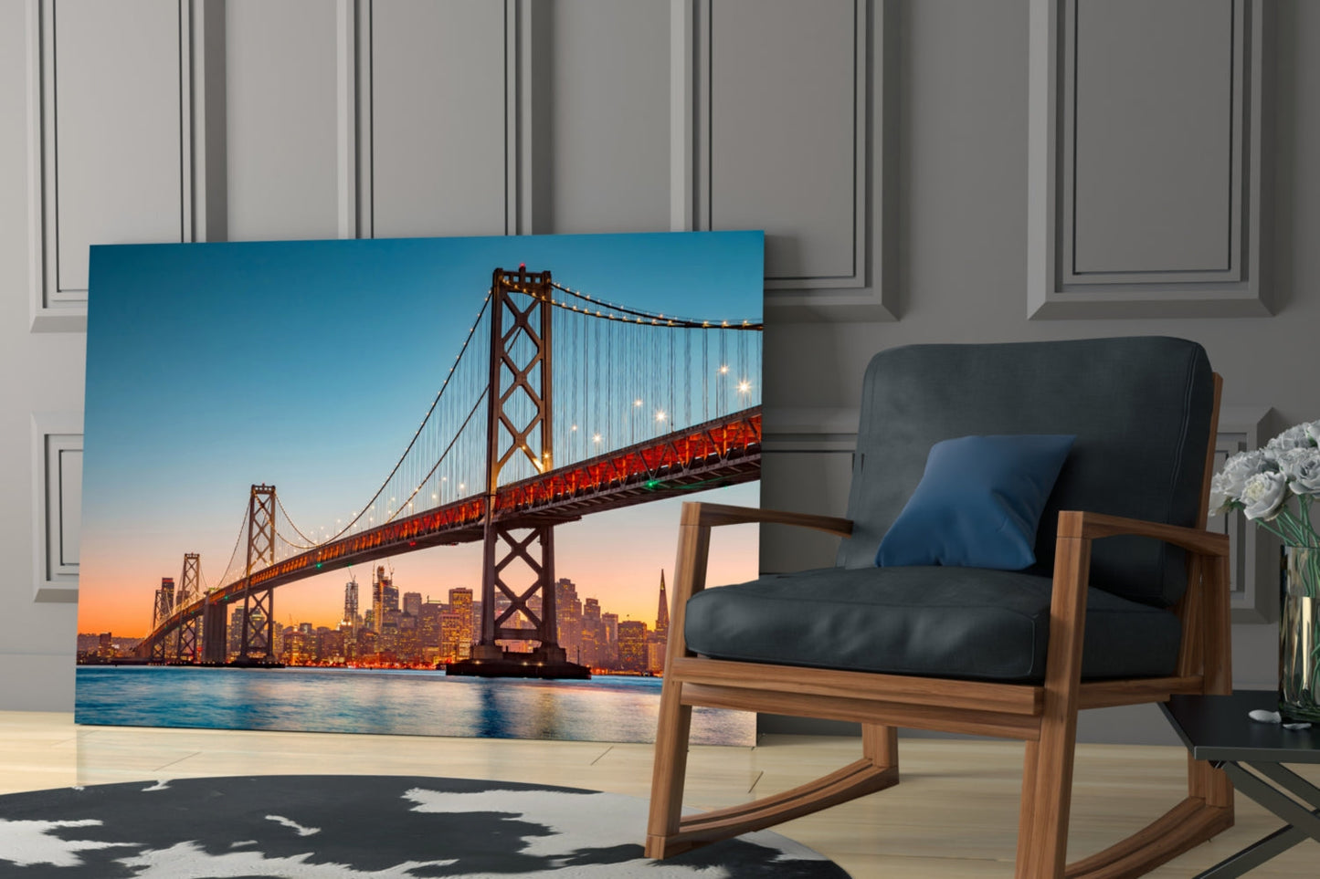 Glass wall art displaying illuminated Bay Bridge at sunset with San Francisco skyline, positioned in modern living room next to wooden chair.