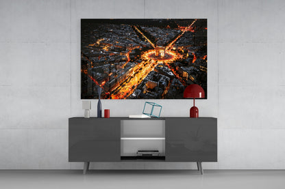 Aerial nighttime cityscape glass wall art displaying illuminated streets and buildings mounted above a dark gray media console with red decorative objects.