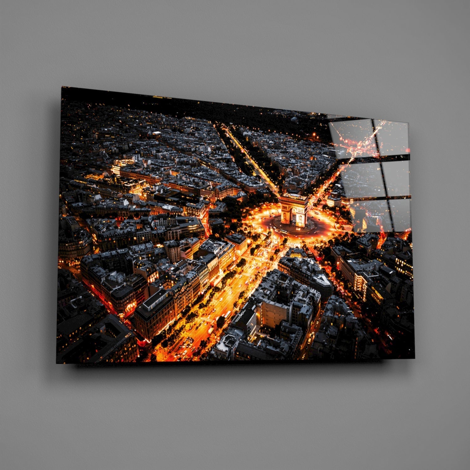 Aerial nighttime photograph of illuminated Parisian streets and buildings printed on segmented glass panels mounted on gray wall.