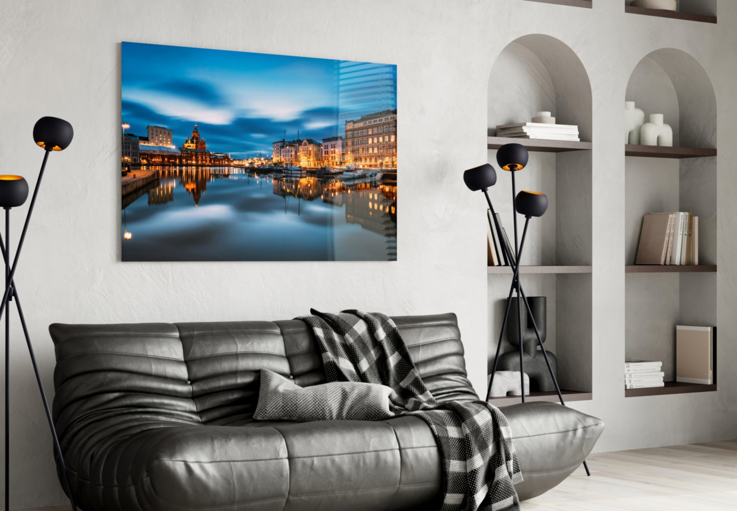 Glass wall art displaying illuminated Helsinki waterfront buildings reflected in calm blue water, hung above gray leather sofa.