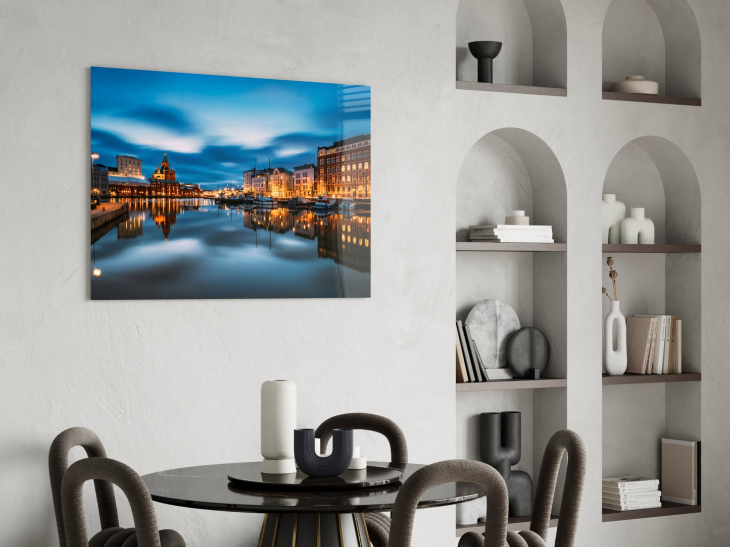 Glass wall art depicting an illuminated European waterfront cityscape at twilight, displayed above a dining table in a modern interior.