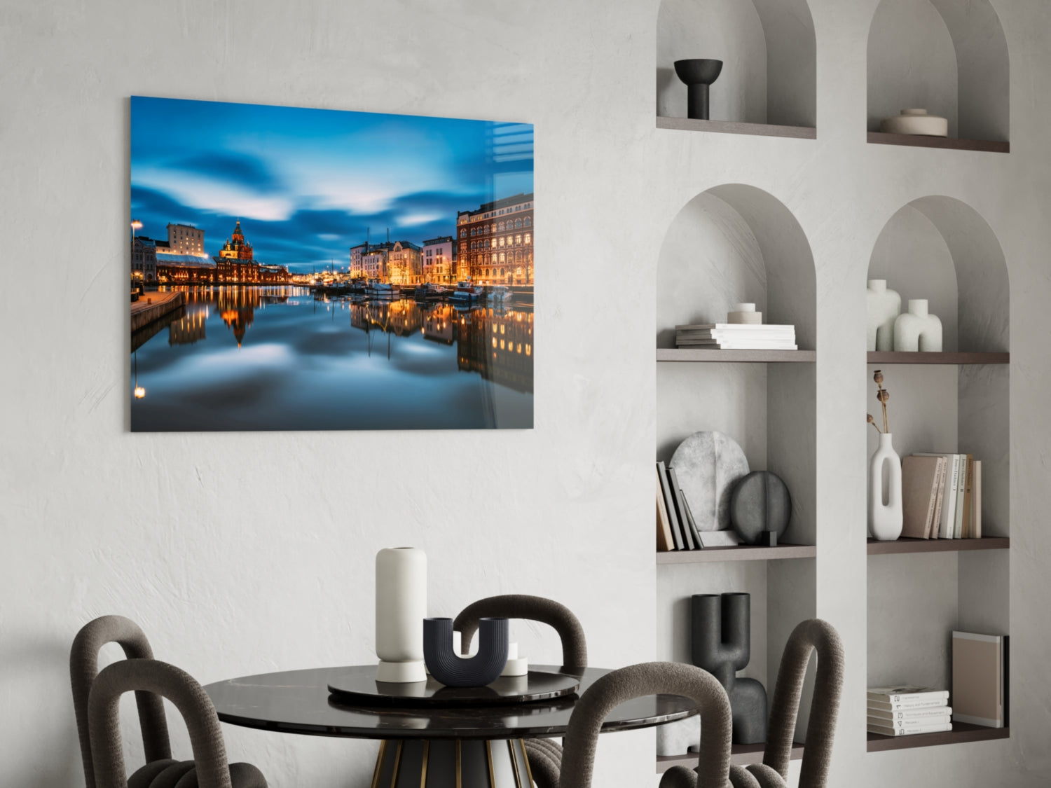 Glass wall art depicting an illuminated European waterfront cityscape at twilight, displayed above a dining table in a modern interior.