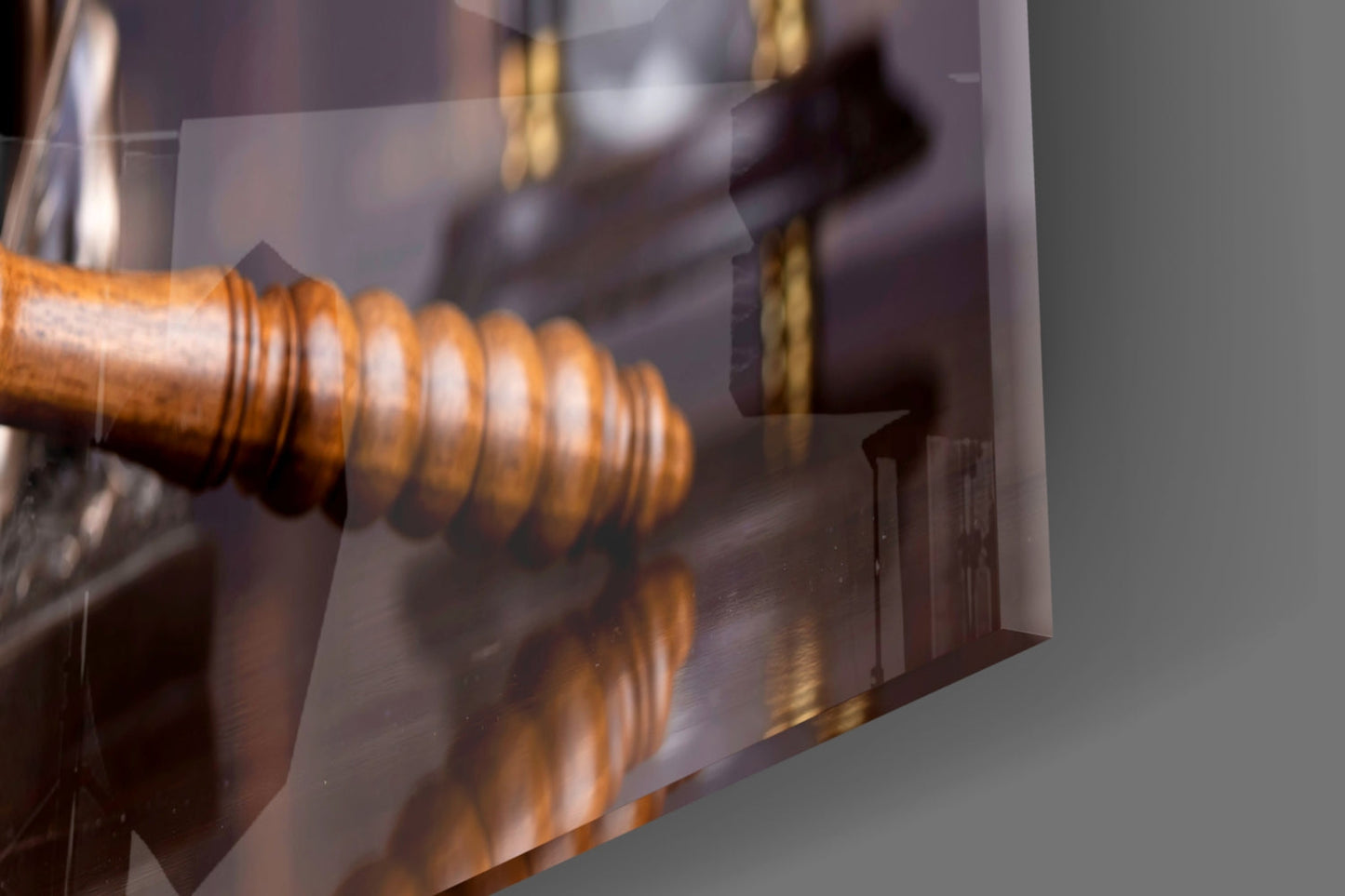 Close-up angled view of wooden gavel with brass bands reflected in frosted glass panel against gray background.