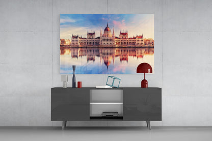 Glass wall art of Hungarian Parliament Building with golden sunset reflection displayed above dark gray media console in modern interior.