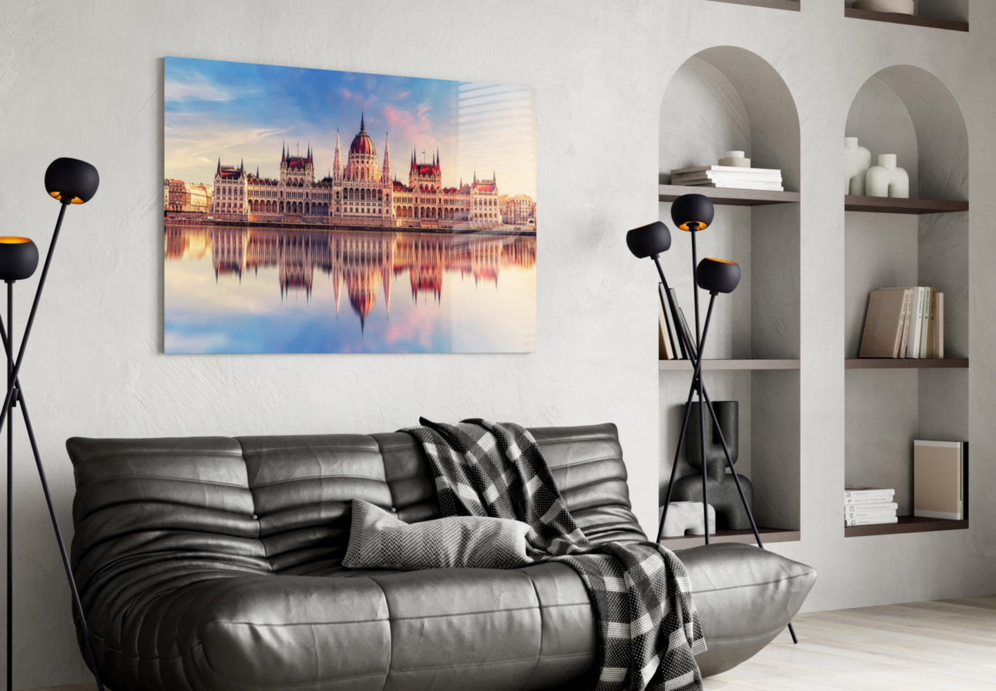 Glass wall art of the Hungarian Parliament Building reflected in water, displayed above a black leather sofa in a modern living room.