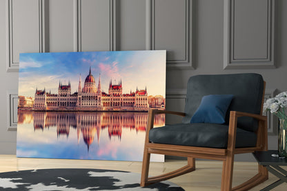 Glass wall art displaying the Hungarian Parliament Building at sunset with water reflections, leaning against a paneled wall beside a wooden chair.