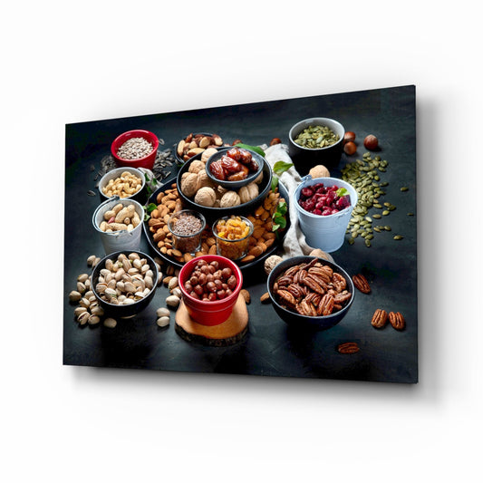 Overhead angled view of glass wall art displaying colorful bowls of mixed nuts, seeds, and dried berries on dark slate surface.