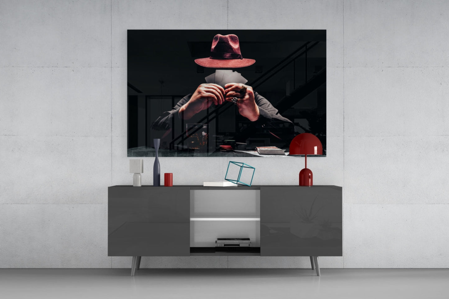 Glass wall art of a mysterious figure in a red hat making a hand gesture, displayed above a modern gray media console in a minimalist interior.