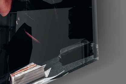 Black glass wall art depicting silhouetted figure in red lighting, displayed on dark shelf with magazines below.