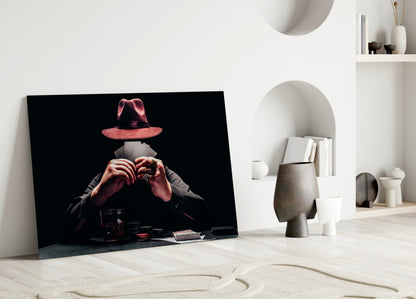 Glass wall art leaning against white wall showing figure in red hat holding cards with black background.
