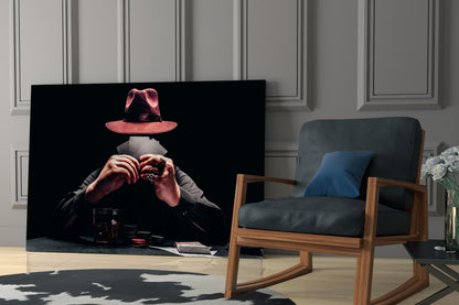 Glass wall art depicting a figure in a red hat and dark jacket holding playing cards, displayed in a modern living room next to a wooden chair.