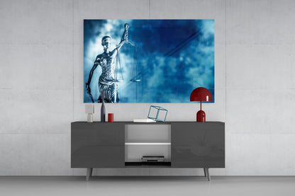 Glass wall art depicting Lady Justice in blue tones displayed above gray media console with red decorative accessories.