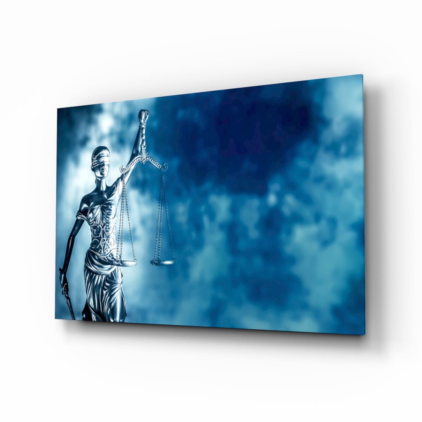 Lady Justice statue with scales displayed on blue glass wall art panel, angled perspective view showing depth and shadow effect.
