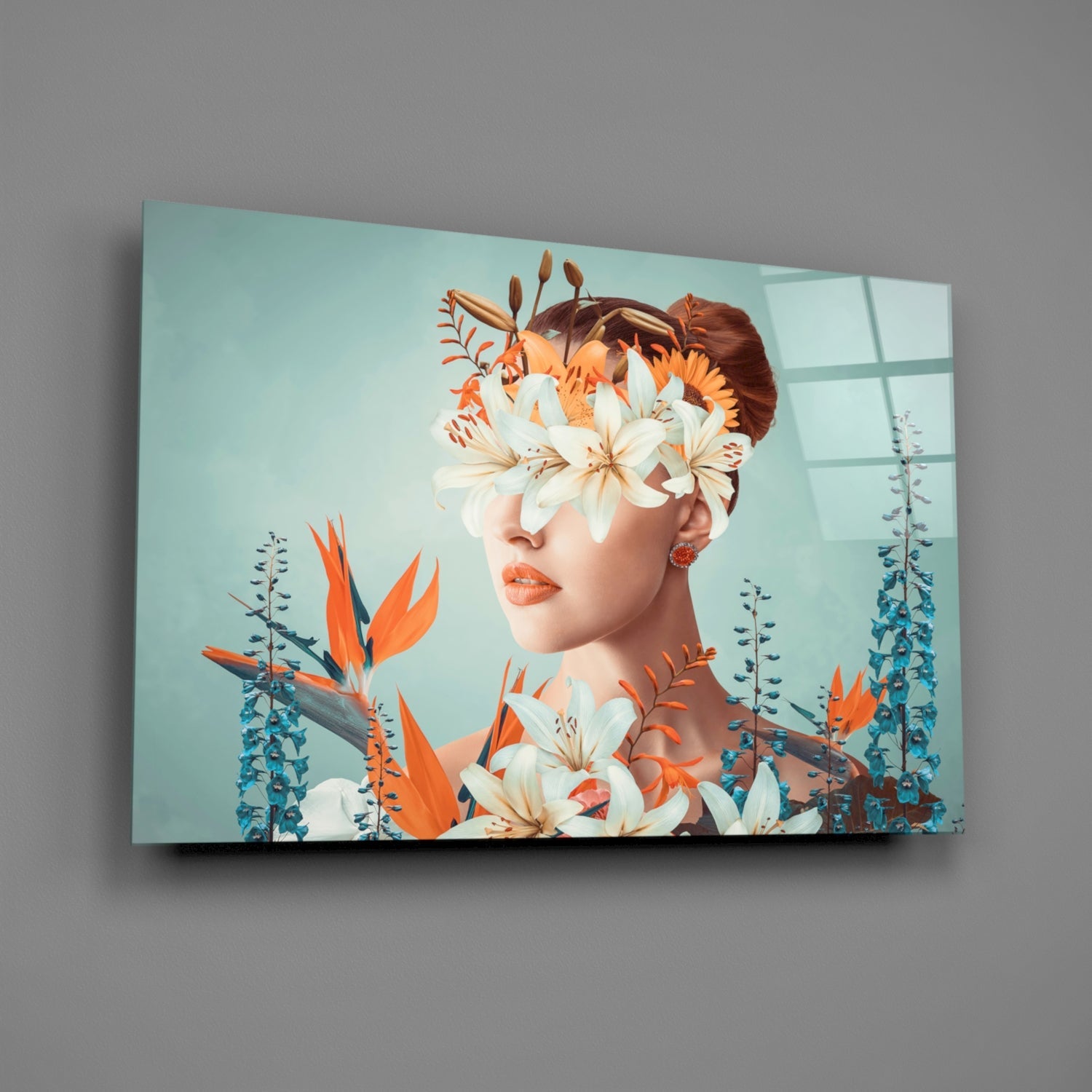 Glass wall art displaying a woman's profile with reddish-brown hair, white and orange flowers covering her eyes, surrounded by blue-green foliage against a pale turquoise background.