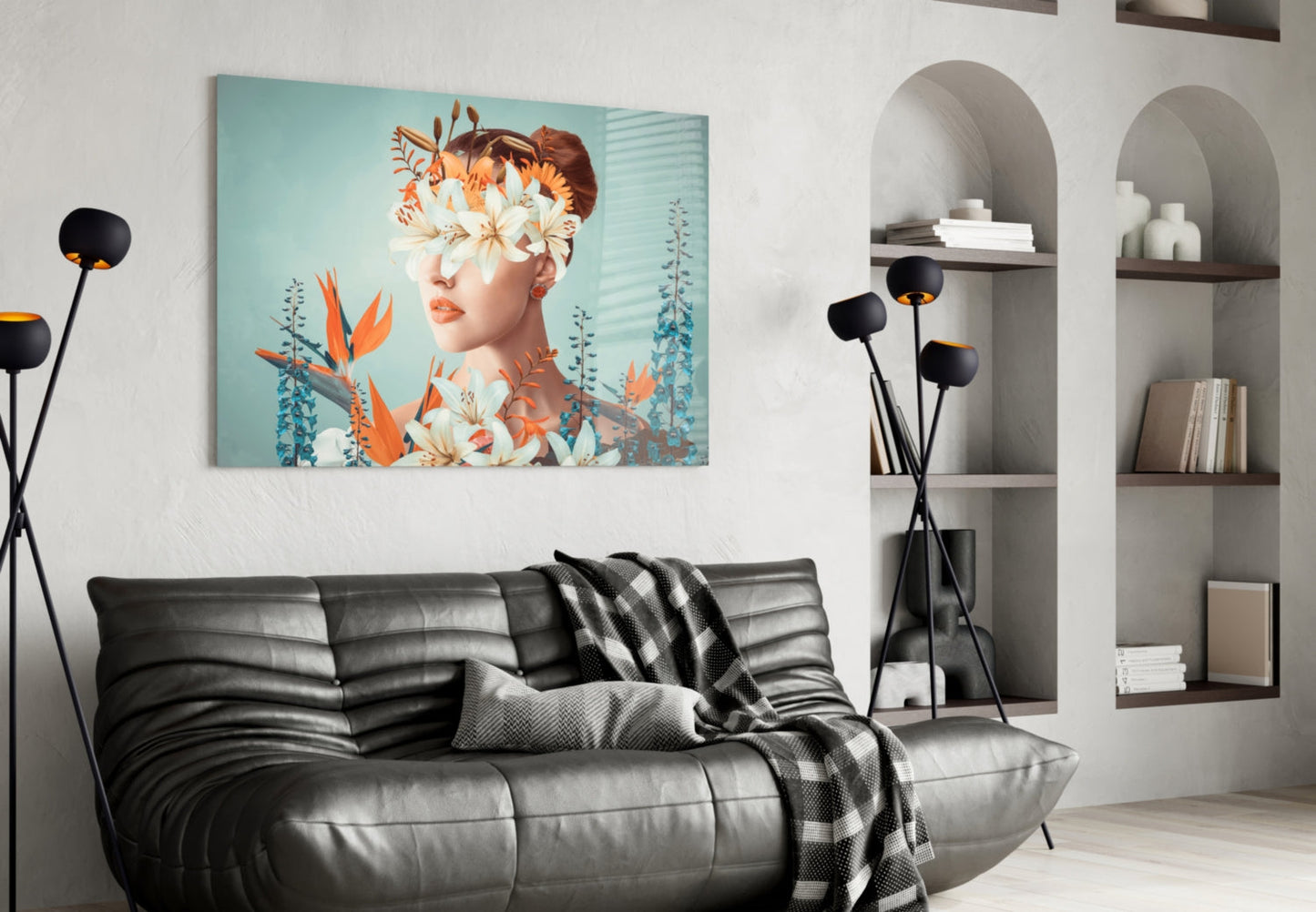 Modern living room with glass wall art depicting woman's face surrounded by orange and white flowers against turquoise background, displayed above black leather sofa.
