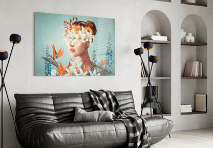 Modern living room with glass wall art depicting woman's face surrounded by orange and white flowers against turquoise background, displayed above black leather sofa.