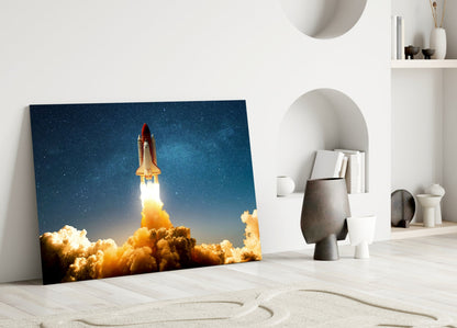 Glass wall art depicting a space shuttle launching through golden clouds against a starry blue sky, displayed in a minimalist white room setting.
