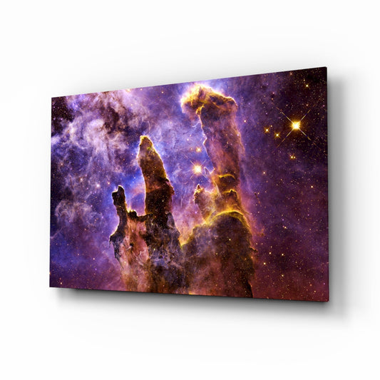 Angled view of glass wall art displaying the Pillars of Creation nebula with purple, gold, and brown cosmic dust formations against a starfield background.