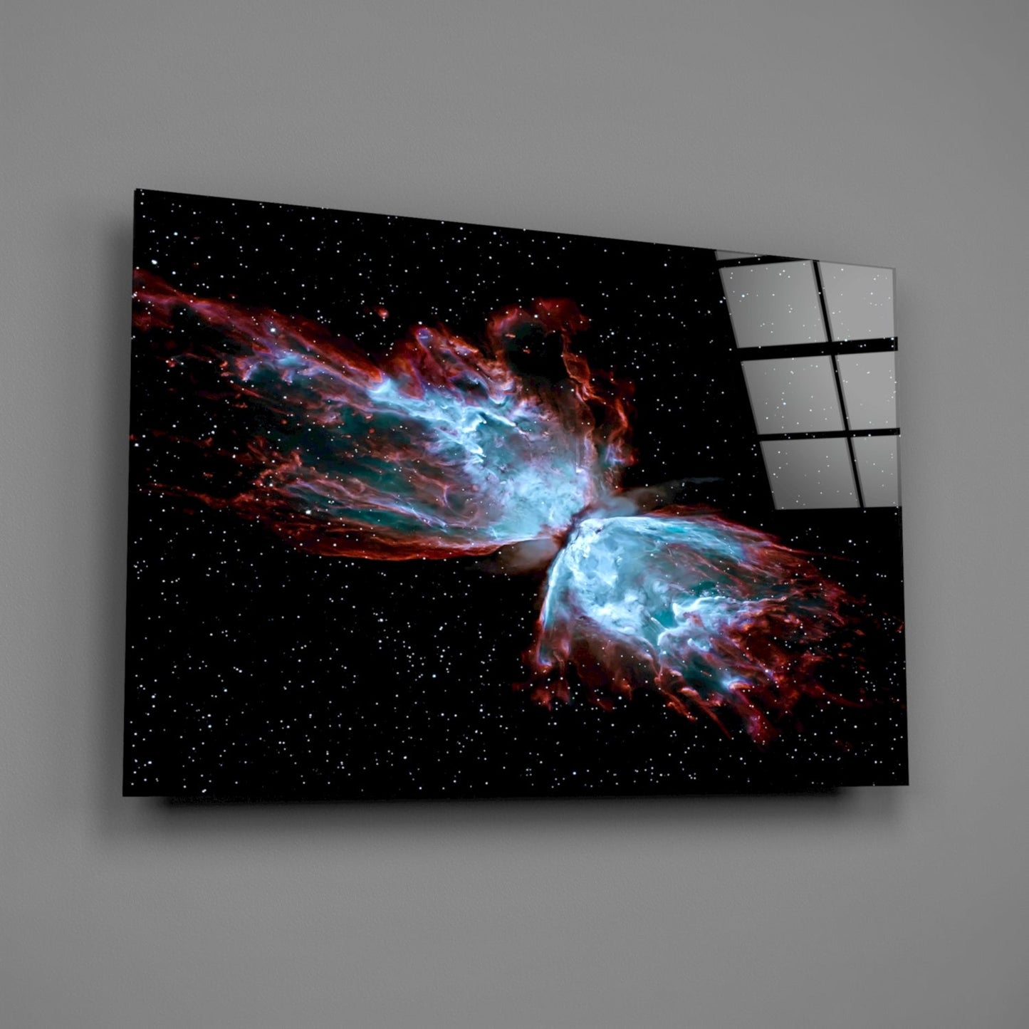 Modern glass wall art displaying a nebula with blue and red cosmic gas clouds against a starry black background, mounted at an angle.