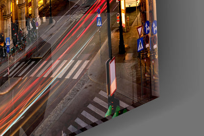 Aerial nighttime view of Vienna street intersection with red vehicle light trails, pedestrian crossing, and blue directional signs on glass surface.
