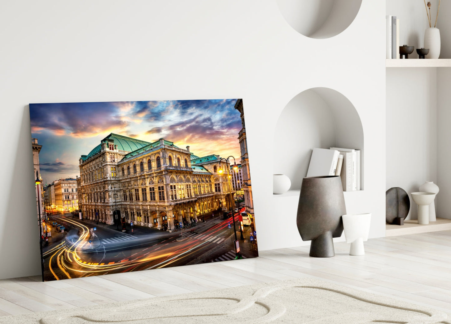 Glass wall art of Vienna State Opera building at sunset displayed on white floor against minimalist white interior with decorative objects.