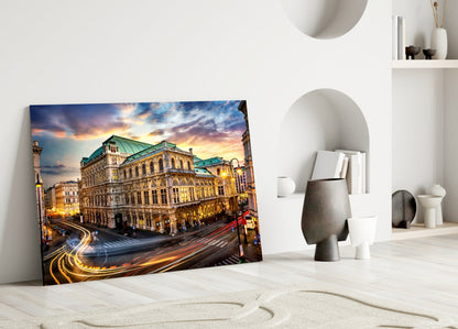 Glass wall art of Vienna State Opera building at sunset displayed on white floor against minimalist white interior with decorative objects.