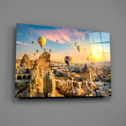 Glass wall art displaying hot air balloons floating above fairy chimney rock formations in Cappadocia at sunset, mounted on gray wall.