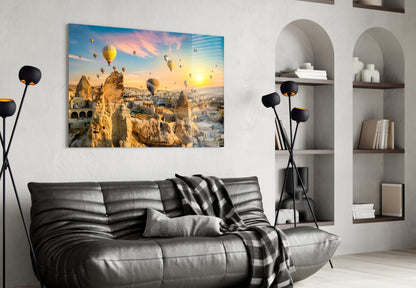 Cappadocia glass wall art displaying hot air balloons over golden rock formations at sunset, mounted above a black leather sofa in a modern living room.