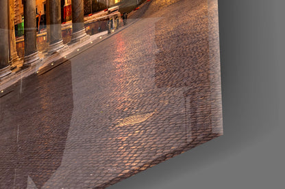 Angled close-up of glass art showing cobblestone street reflection with warm golden light on building facade.