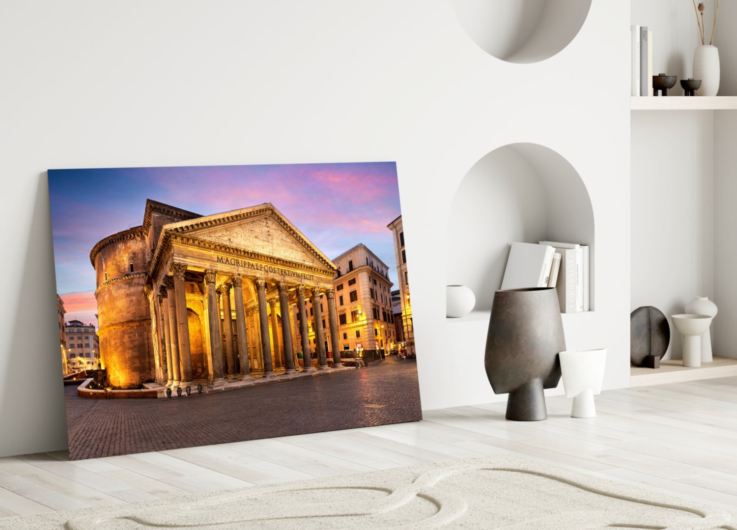 Pantheon glass wall art leaning against white wall in minimalist room with sand sculpture and ceramic vessels.
