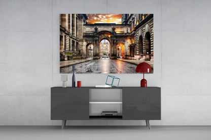 George Square Glass Wall Art displayed above a dark grey TV console, showing an illuminated European courtyard at sunset with architectural arches.