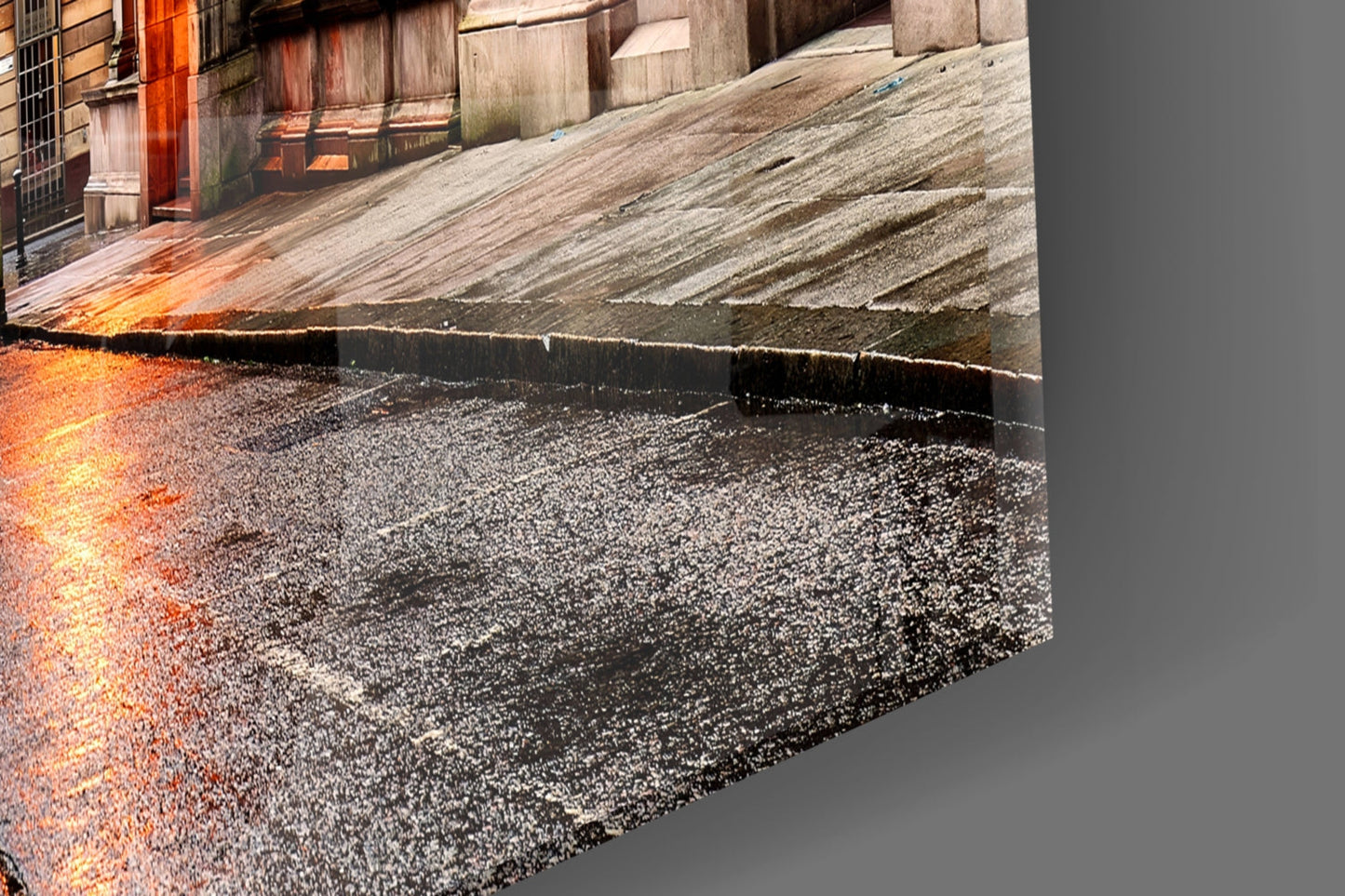 Close-up detail of glass wall art showing textured asphalt surface with orange industrial building and concrete structures in background.