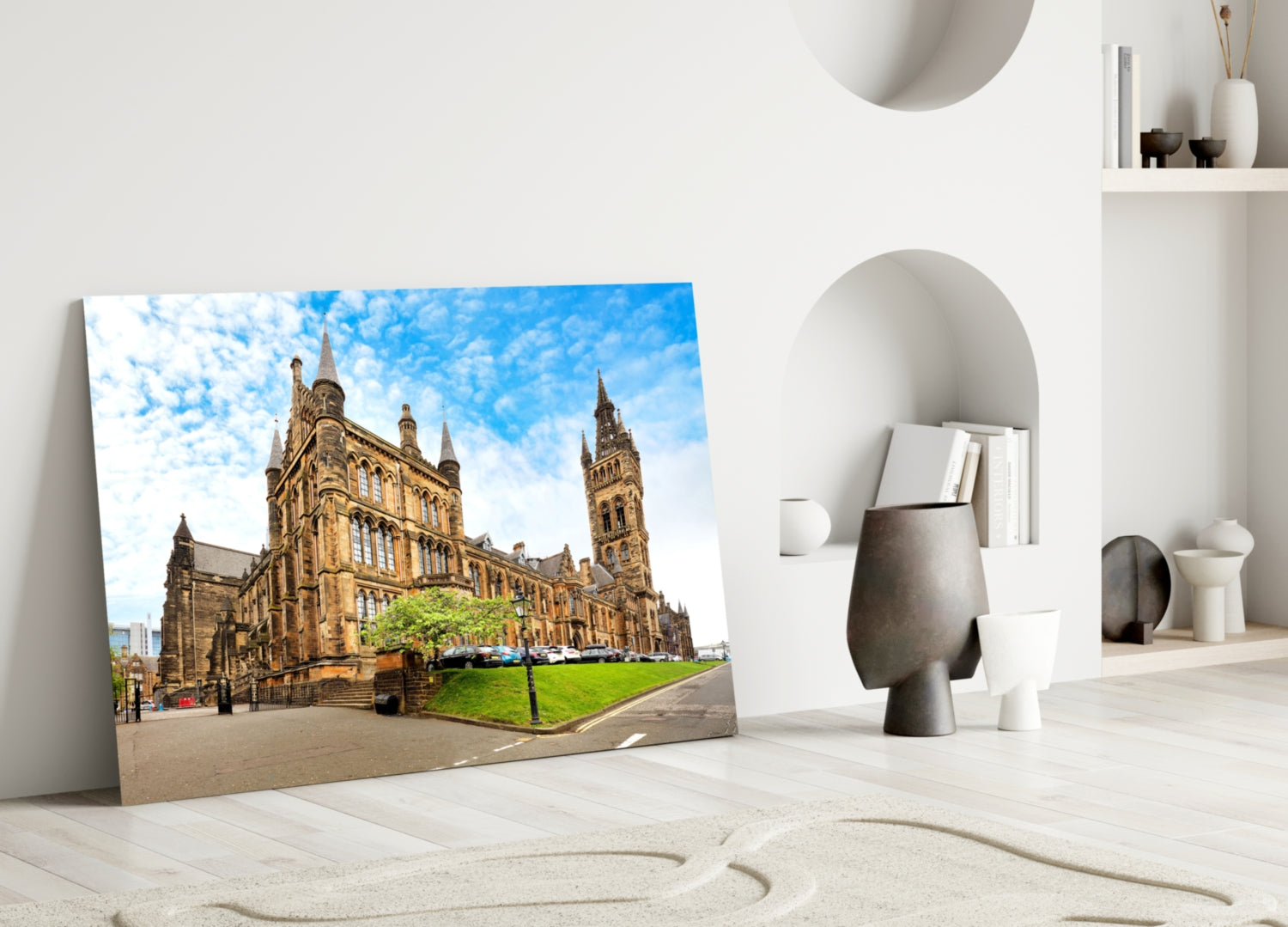 Glass wall art displaying Glasgow University's Gothic architecture building with blue sky, leaning against white wall beside decorative objects.