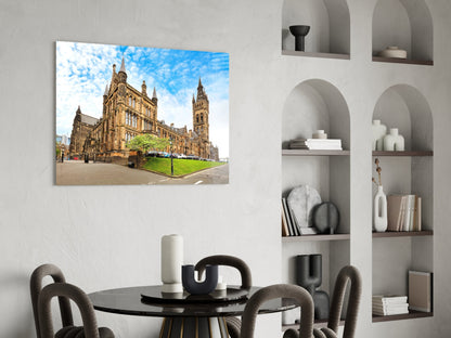 Glass wall art depicting golden University of Glasgow Gothic building with blue sky, displayed above round black dining table.