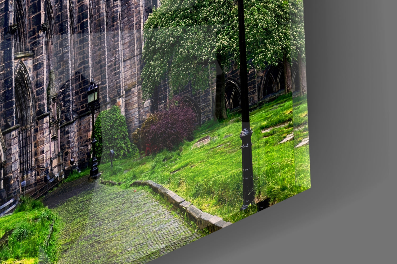 Angled view of glass wall art showing ivy-covered stone cathedral walls with green lawn and black lamp post in foreground.